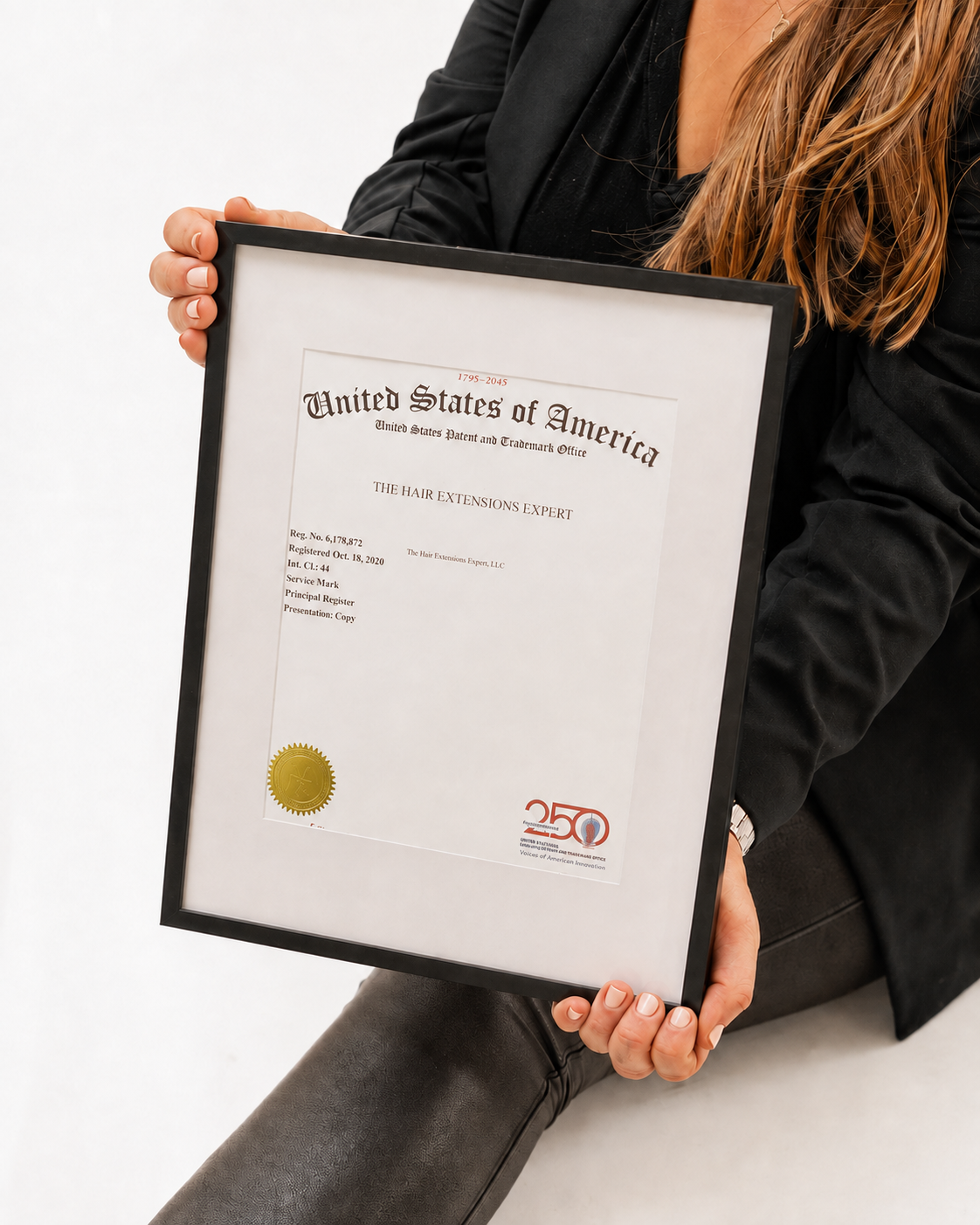 Lauren holding her framed The Hair Extensions Expert trademark certificate with a gold seal